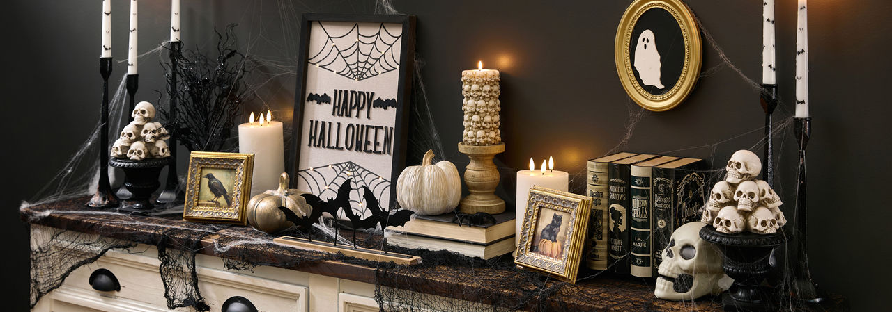 A spooky Halloween-themed foyer table is decorated with classic Halloween decorations from pOpshelf featuring skeletons, Halloween skulls, moody gothic-inspired framed art, bat candlesticks, a spider web tablecloth, golden pumpkins, and more affordable Halloween themed finds.