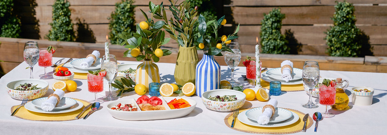 Outdoor dining table set with bright, colorful serveware, coastal Italian themed decor, affordable serving platters, and pops of lemon decorations from pOpshelf.
