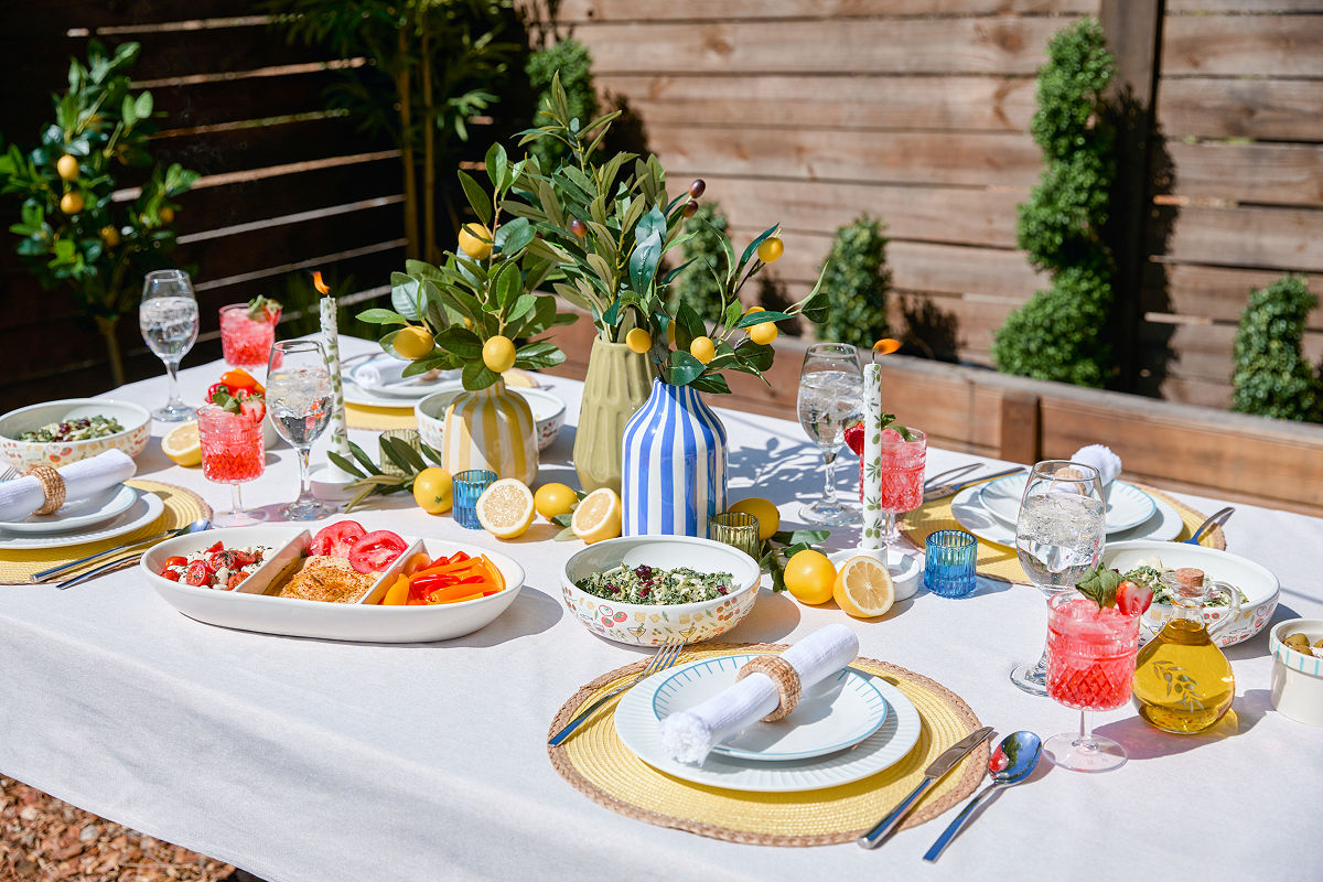 Outdoor dining table set with bright, colorful serveware, coastal Italian themed decor, affordable serving platters, and pops of lemon decorations from pOpshelf.